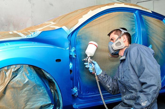 Worker painting blue car.